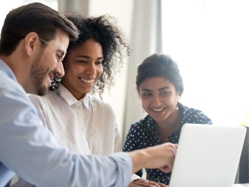 One male and two female students looking at a laptop screen together.