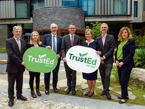 Jim Murray (QQI Director of Development), Laura Harmon (Executive Director, Irish Council for International Students), Dr Padraig Walsh (QQI CEO), Minister Patrick O'Donovan, Professor Irene Sheridan (QQI Chair), Bryan Maguire (QQI Director of Integration) and Mary Grennan (QQI Head of International Education) stand in a line holding TrustEd Ireland signs at the launch of the new quality scheme.