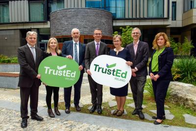 Jim Murray (QQI Director of Development), Laura Harmon (Executive Director, Irish Council for International Students), Dr Padraig Walsh (QQI CEO), Minister Patrick O'Donovan, Professor Irene Sheridan (QQI Chair), Bryan Maguire (QQI Director of Integration) and Mary Grennan (QQI Head of International Education) stand in a line holding TrustEd Ireland signs at the launch of the new quality scheme.