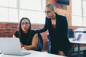 Two young businesswomen working together in a creative office. Female colleagues using a laptop together while working on a new project. Businesswomen teaming up and sharing ideas.