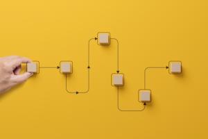 Hand holding wooden cube block arranging processing management on yellow background.